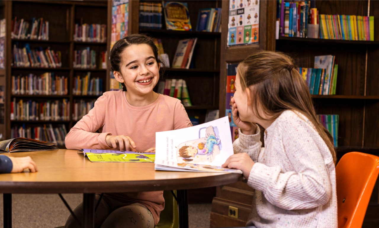 Two girls sitting in a library and laughing